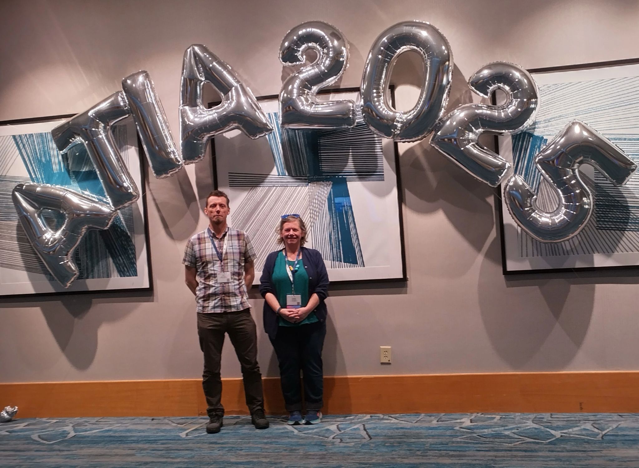 Fil McIntyre (left) and Claire Harrison (right) pictured standing under large silver foil balloons that say ATIA